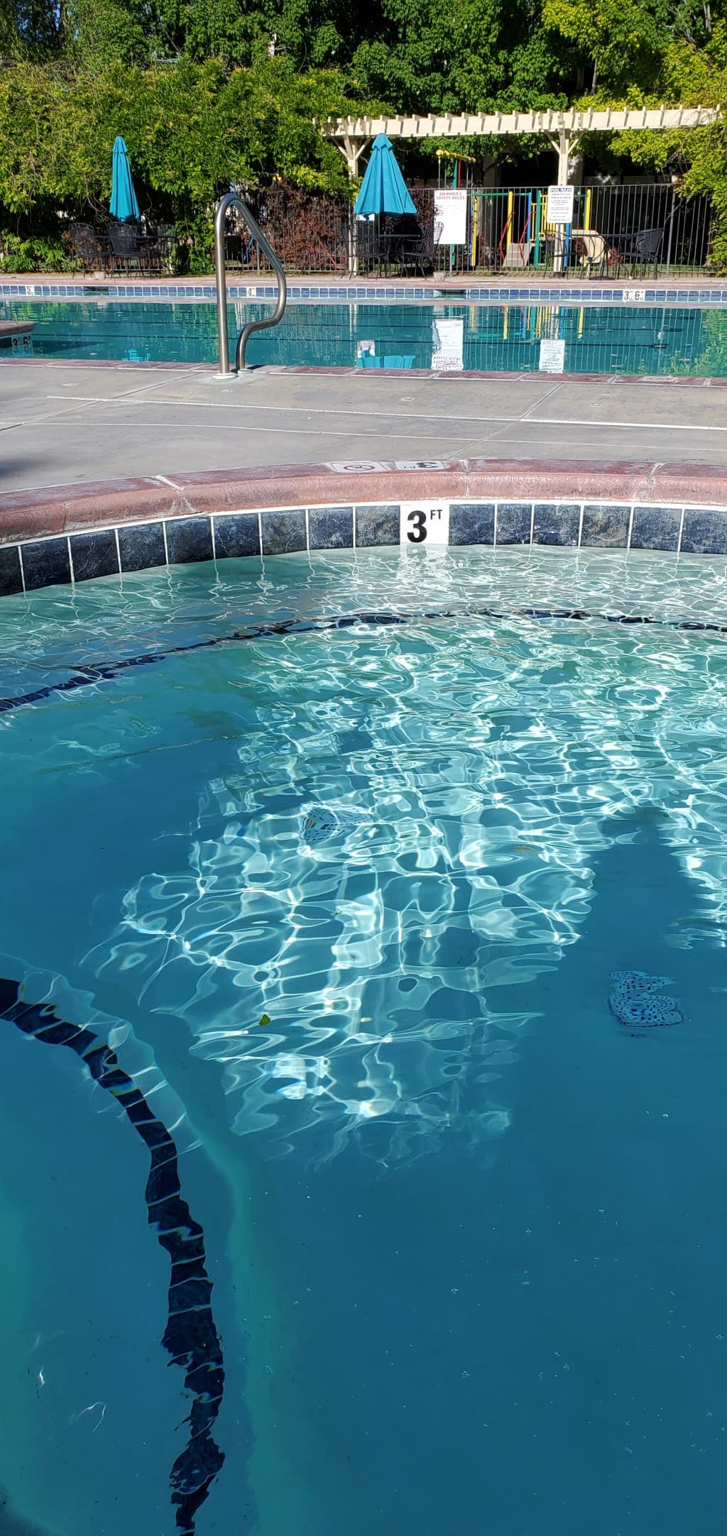 A shallow pool/spa with a large pool in the background